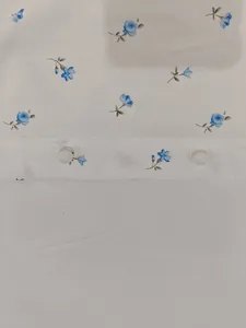 Dettaglio ravvicinato di tessuto bianco con piccole stampe floreali blu e bottoni