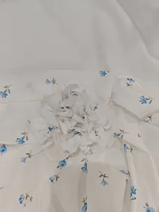 Dettaglio di un abito bianco con scollo a V, stampa floreale blu e fiore in tessuto 3D.