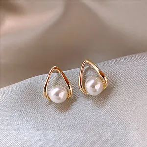 Minimalist gold teardrop stud earrings with white pearl center on silk background