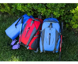 Large red and blue outdoor hiking backpacks shown with trekking poles and gear on grass.