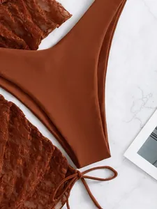 Dettaglio ravvicinato di set bikini in pizzo a rete marrone e tessuto liscio su marmo
