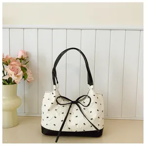 Detailed view of textured white underarm bag featuring embroidered black bows and ribbon