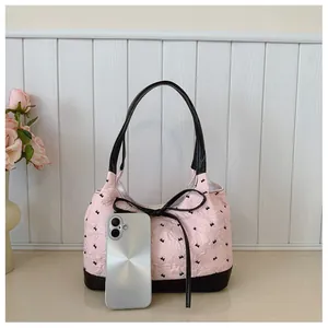 Detailed view of pink underarm bag with black bow pattern and phone for size reference