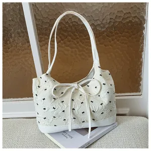 Detailed view of a white shoulder bag with black bow embroidery and ribbon accent.