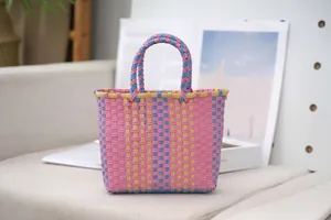 Hand-woven plastic tote bag with pink and blue color-blocking shown on a cozy sofa