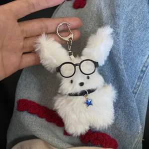 Handheld detail of a cute white fuzzy plush rabbit keychain wearing black glasses and star charm