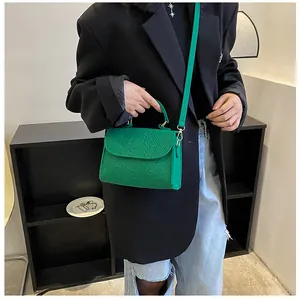 Close-up of green snake-skin textured handbag worn crossbody over a black blazer.