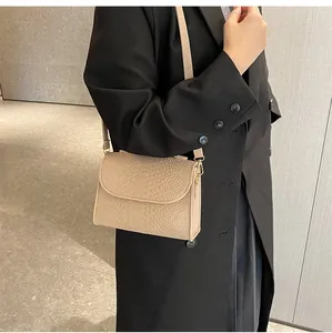 Close-up of a beige snakeskin pattern small square crossbody bag worn with a black blazer