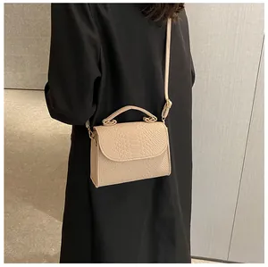 Close-up detail of a beige snakeskin texture crossbody bag styled with a black coat.