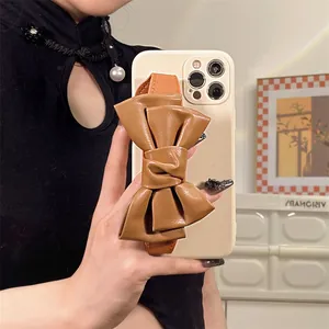 Elegant iPhone case with large brown leather bow wristband and cream-colored finish.