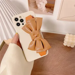Close-up of a stylish cream iPhone case featuring a large tan leather bow wrist strap