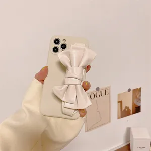 Cream-colored iPhone case featuring a large leather-like bow wristband for secure grip.