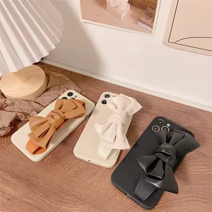 Detail view of stylish bow wristband phone cases in brown, cream, and black colors.