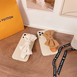 Close-up of cream and tan leather bow wristband phone cases for iPhone on a wooden desk.