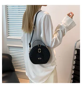 Fashionable black round quilted crossbody bag worn by a model in a white shirt