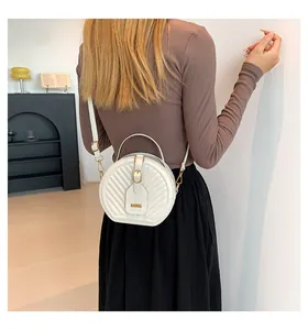 Rear view of model wearing a stylish white quilted circular crossbody bag with gold hardware.