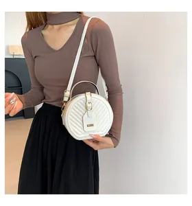Model carrying a stylish white circular crossbody bag with diagonal textured patterns
