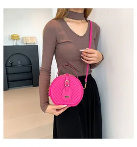 Close-up detail of a hot pink round crossbody bag with chevron quilting on model