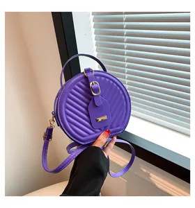 Close-up of a purple quilted round crossbody bag held by a hand in detail view