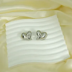 Macro detail of large silver liquid metal heart stud earrings on a wavy white tray