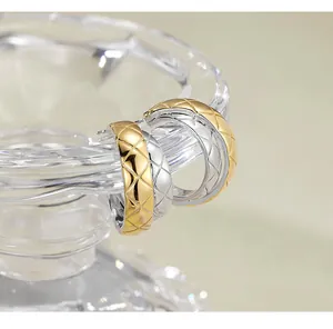 Close-up detail of luxury silver and gold quilted hoop earrings on a clear glass display stand