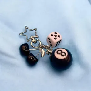 Close-up of cherry and 8-ball dice keychain with star-shaped metal clasp on blue fabric