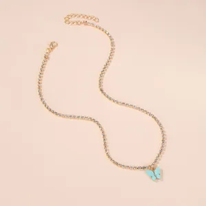 Detail shot of a minimalist gold butterfly necklace with rhinestones on beige background