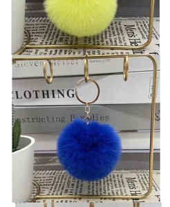 Close-up of electric blue 8cm faux fur pom pom keychain on gold display stand.