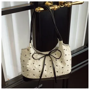 Detail of white textured underarm bag with black bow embroidery and large bow tie