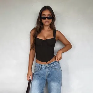 Model wearing black lace trim corset camisole top with blue jeans against a gray wall