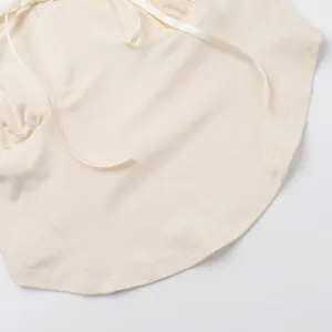 Macro detail of a cream camisole's bottom hem featuring elegant ribbon accents