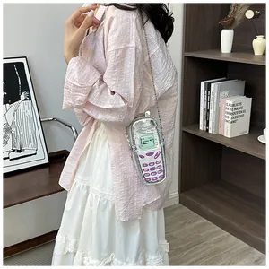 Mini silver retro telephone shaped crossbody bag worn by a model in a stylish room