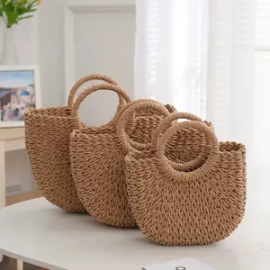 Close-up of three different sizes of round handle paper straw bags on a white table