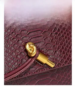 Detailed macro shot of wine red snake skin textured handbag with unique gold knot metal clasp.