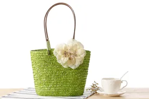 Detail of a vibrant green woven straw beach handbag with a large decorative flower