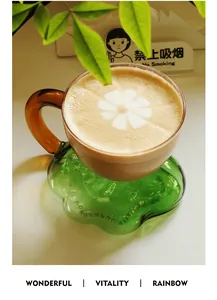 Latte coffee in a glass cup on a green cloud-shaped coaster with latte flower art