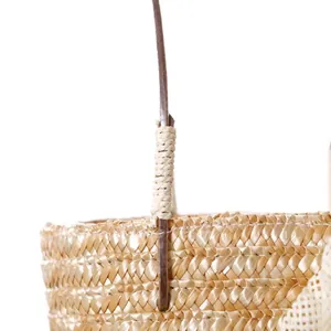 Detail view of woven handle attachment on a handmade straw beach handbag for women