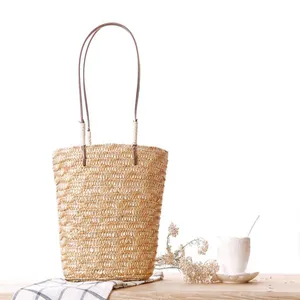 Elegant handwoven straw tote bag with thin brown straps displayed on a rustic wooden table.