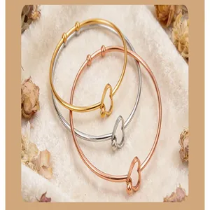 Close-up of three minimalist heart-shaped open bangles in gold, silver, and rose gold.