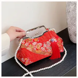 Macro detail of red Chinese style embroidered kiss-lock bag featuring elegant pearl strap.