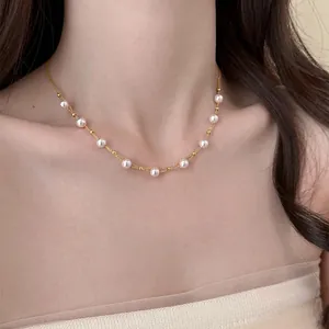Detail of an 18k gold plated necklace with delicate pearls on a woman's collarbone.