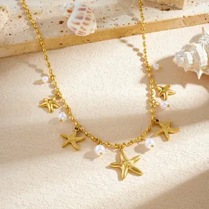 Détail du collier étoile de mer doré avec perles blanches sur fond de plage sablonneux.