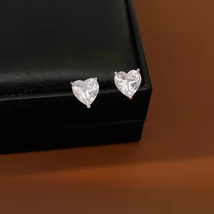 Macro view showing sparkling heart-shaped zircon earrings on a luxury black jewelry box.