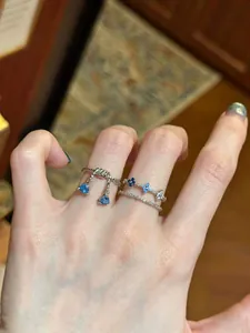 Close-up of a hand wearing silver rings with blue triangle and flower-shaped zircons.