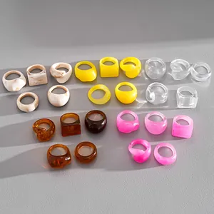 Collection of colorful geometric resin rings in square and round shapes on grey background