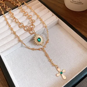 Close-up of vintage gold layered necklace with emerald green stone and cross pendant in tray.