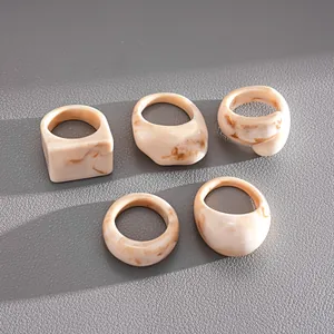 Detailed view of 5 chunky resin rings with cream marble pattern on leather surface