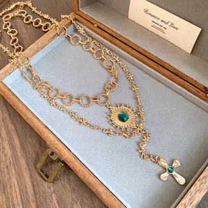 Vintage gold layered necklace with sunburst and cross pendants featuring green gems