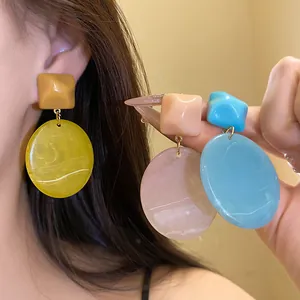 Close-up of colorful resin drop earrings in yellow, pink, and blue.