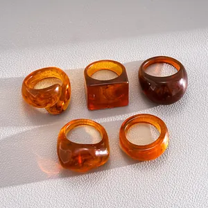 Macro view of five amber resin rings in geometric shapes on a textured surface.